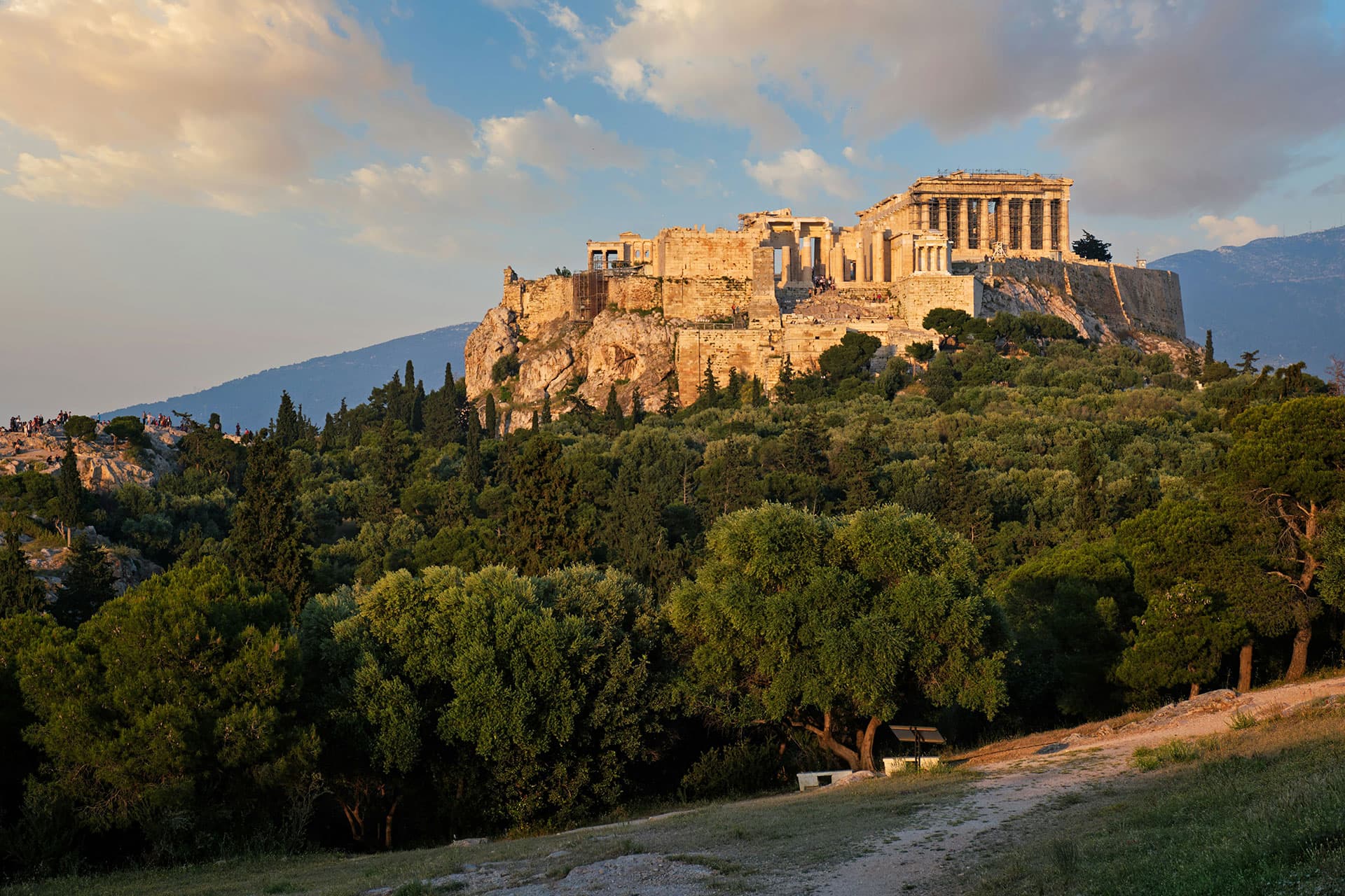 The Acropolis of Athens at sunset, seen across a pine-covered hill